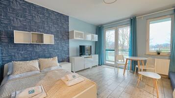 Habitación de hotel con cama, televisión, escritorio, sillas y balcón con vistas.