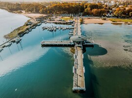 Vista aérea de un puerto deportivo con barcos amarrados, un muelle que se extiende hacia el agua y un edificio con techo circular.