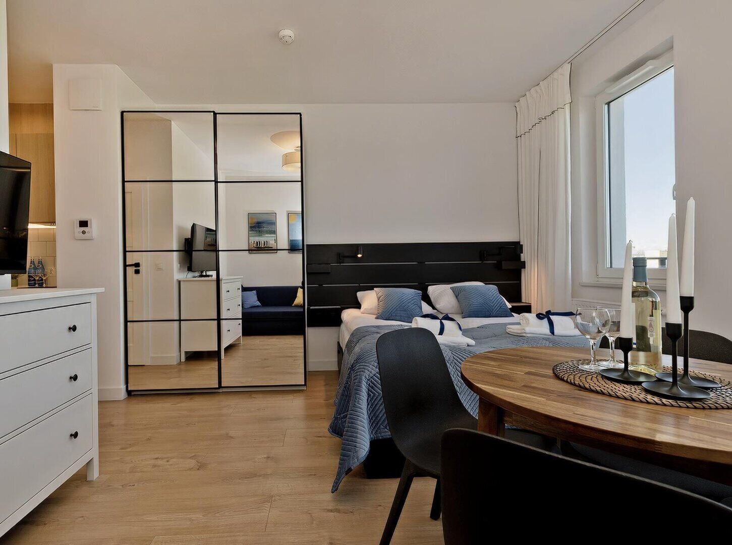 Een moderne hotelkamer met een bed, nachtkastjes, een televisie, een zithoek met een tafel en stoelen, en een groot raam.
