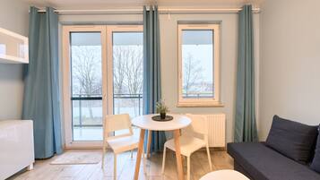 Una habitación moderna con sofá, una mesa de comedor con sillas, radiador y ventanas grandes con cortinas.
