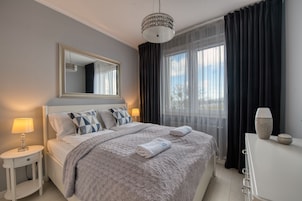 Un dormitorio ordenado con cama, mesitas de noche, un espejo y una ventana con cortinas.