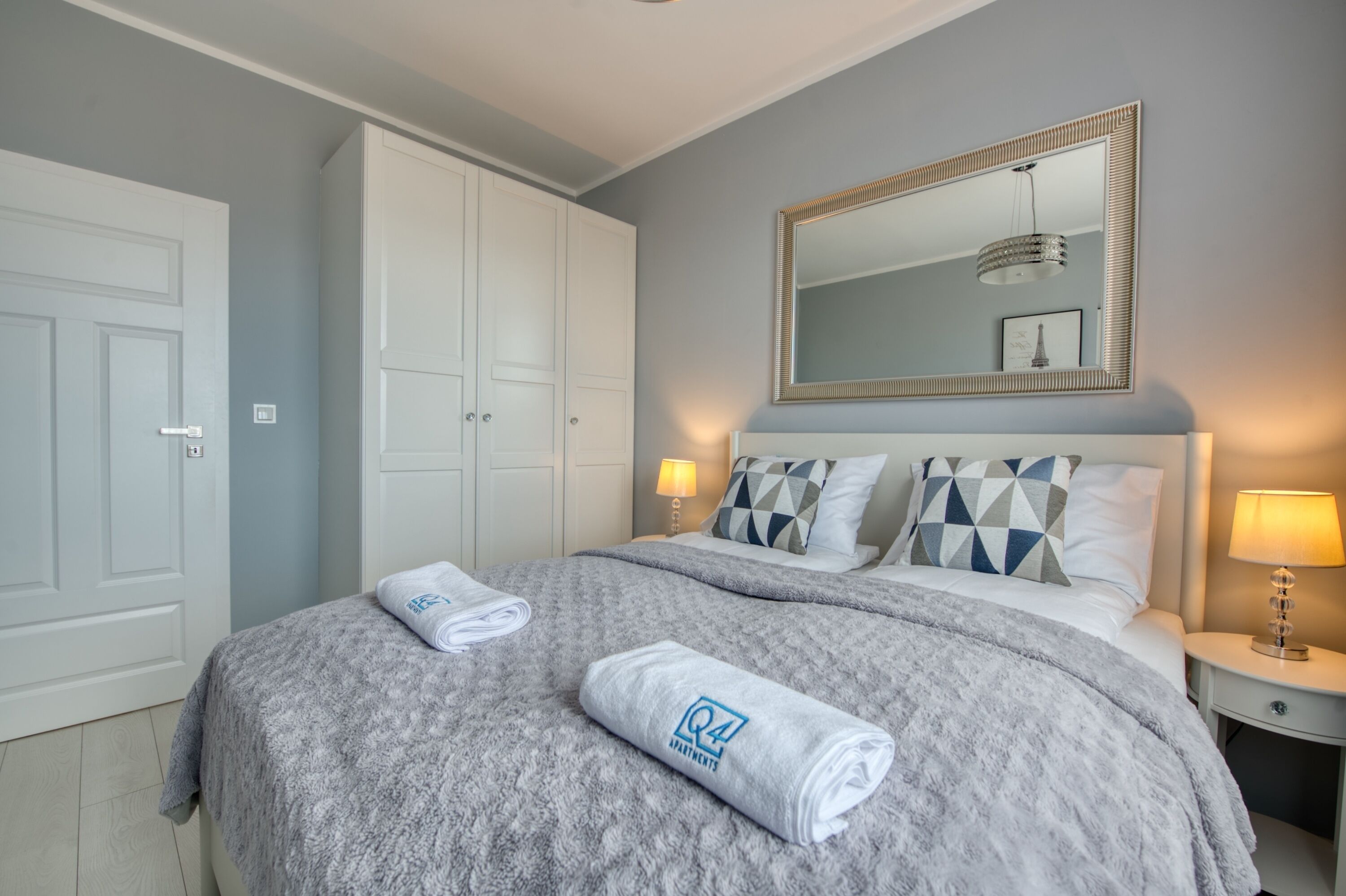 A bedroom with a bed, a large mirror, two bedside lamps, and a wardrobe.