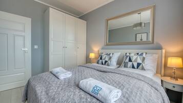 A bedroom with a bed, a large mirror, two bedside lamps, and a wardrobe.