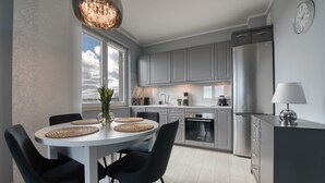 A modern kitchen with grey cabinets, a stainless steel refrigerator, and a dining area with a round table and chairs. - Apartamenty NEXO - Puck by Q4Apartments  (Puck)