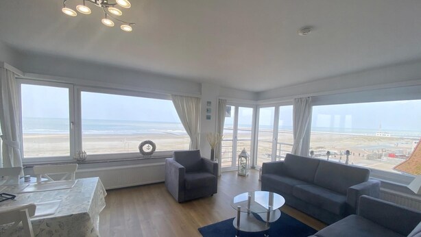 A spacious living room with a view of the beach, a dining area, and a seating area with a coffee table.