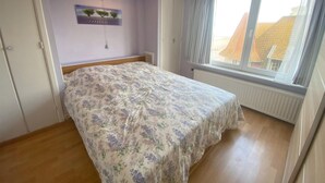A bedroom with a bed, a window with curtains, a radiator, and a ceiling light.