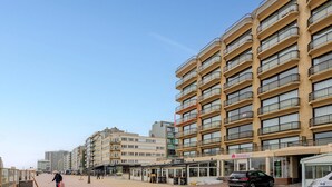 Ein mehrstöckiges Hotel mit Balkonen, ein Erdgeschoss mit Geschäften und einem wolkenlosen Himmel.