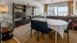 Ein modernes Wohnzimmer mit Essbereich, einer Couch, einem Fernseher und Blick auf den Strand.