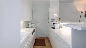Een smalle keuken met witte kastjes, een houten vloer en een klein aanrecht met een koffieapparaat en een lamp.