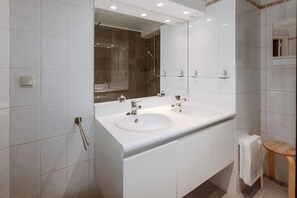 A modern bathroom with two sinks, a glass shower enclosure, and a small wooden stool.