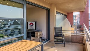 Un balcon avec une table et des chaises, une enseigne indiquant « ERA Real Estate Servivo », et une vue sur les bâtiments à travers de grandes fenêtres.