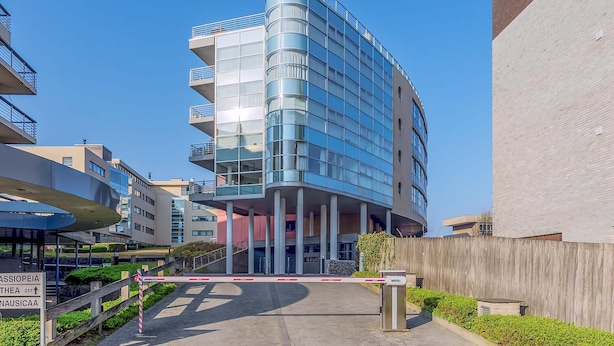 Un bâtiment moderne à la façade incurvée, doté de nombreux balcons et d’une entrée sécurisée par un portail.