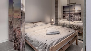 Une chambre moderne avec un grand lit, une table de chevet avec une lampe et un grand miroir qui reflète la pièce.