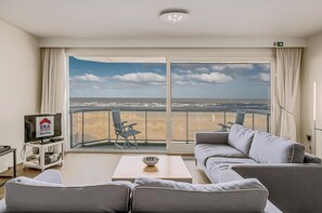 A modern hotel room with a large balcony, a sofa, a coffee table, and a TV on a stand. - Gray D´Albion A53 + G (Oostduinkerke)