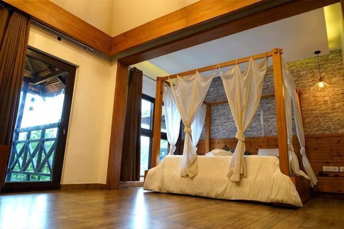 A four-poster bed with a canopy, wooden beams, and a stone wall.