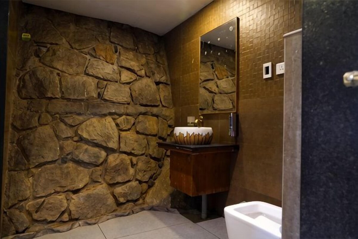 A bathroom with a stone wall, a wooden vanity, a mirror, and a white sink.