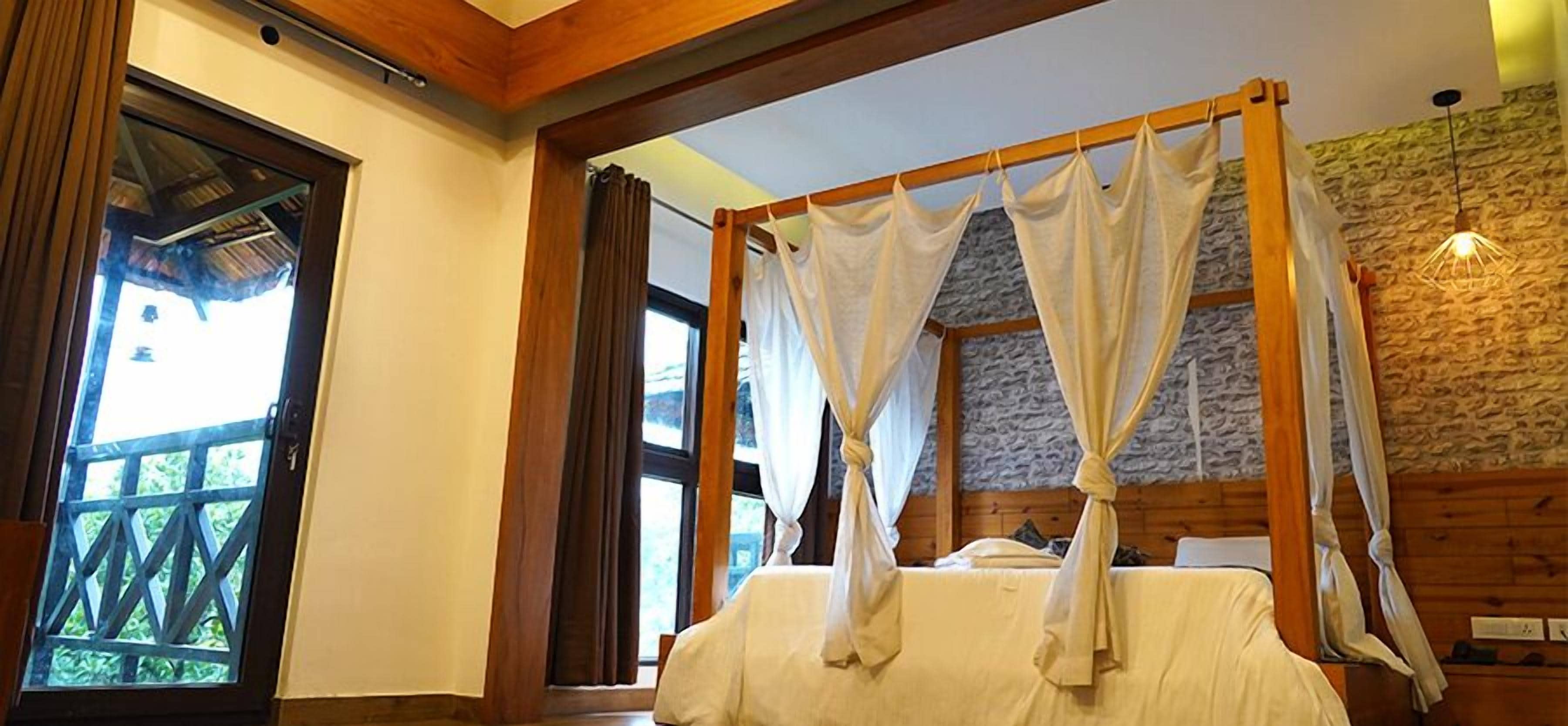 A room with a four-poster bed, wooden beams, and a stone wall.