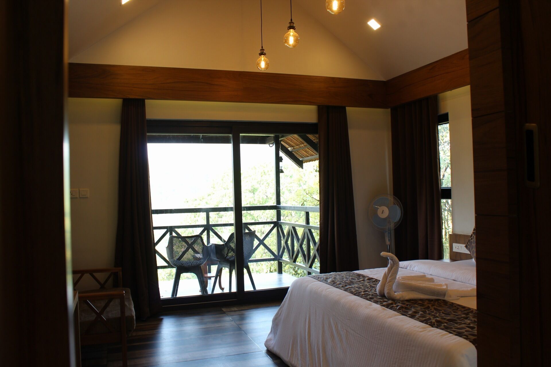 Une chambre d’hôtel avec un lit, un ventilateur et un balcon équipé de chaises.