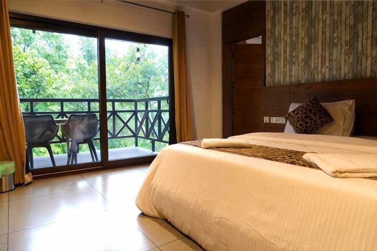 Ein Schlafzimmer mit einem großen Bett, einem Balkon mit Tisch und Stühlen und Blick auf Grünflächen.