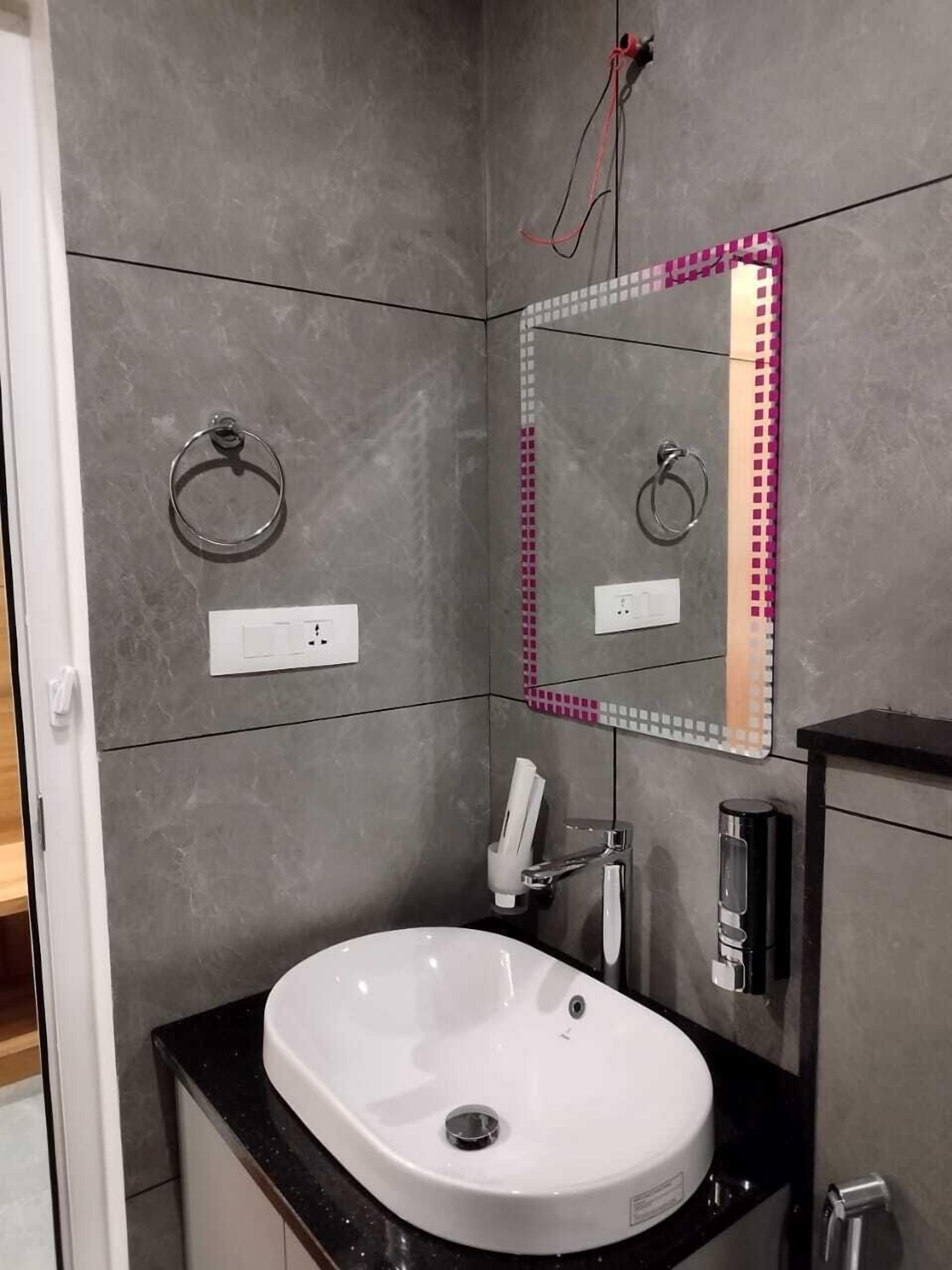 Un bany modern amb un lavabo blanc, un mirall amb vinga rosa i un penjador de tovalloles a la paret.
