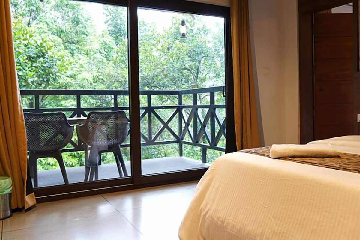 Ein Schlafzimmer mit einem Bett, Blick ins Grüne durch eine Schiebetür und ein kleiner Tisch mit Stühlen draußen.
