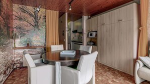 A dining area with a round table and white chairs, a kitchen with cabinets, and a mural on the wall.