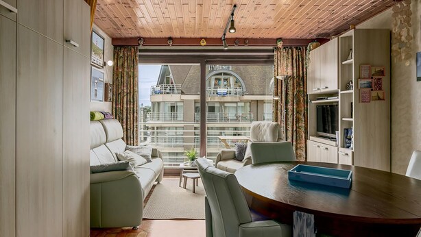 A modern living room with a sofa, chairs, a dining table, and a view of a building through large windows.