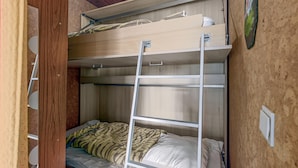 A bunk bed room with a ladder, wooden walls, and a small white shelf.