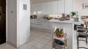 Et moderne køkken med hvide skabe, en central ø med barstole og diverse hårde hvidevarer.