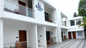 Een modern hotel met een witte gevel, meerdere balkons en een betegelde binnentuin.