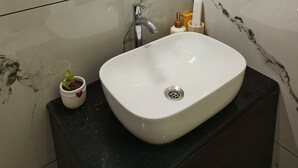 Een badkamer met een wit wastafelmeubel, een ronde spiegel, een moderne kraan en een potplant.