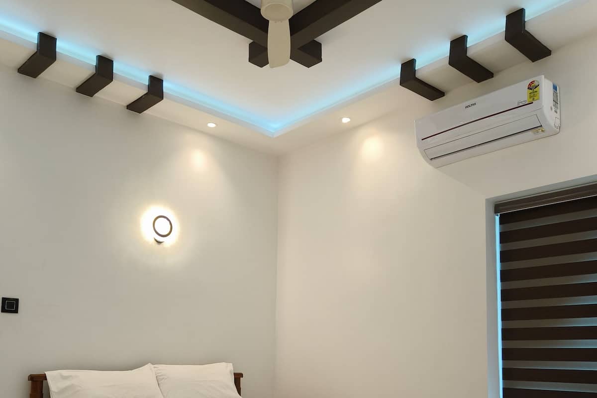 A bedroom with a wooden bed, white bedding, a ceiling fan, recessed lighting, an air conditioning unit, and a window with blinds.