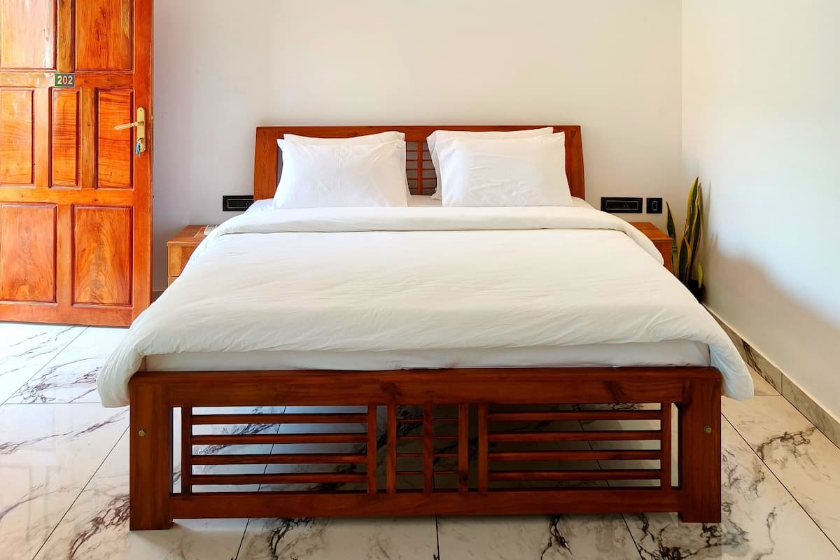 A neatly made bed with a wooden headboard, a ceiling fan, recessed lighting, and a marble-tiled floor.