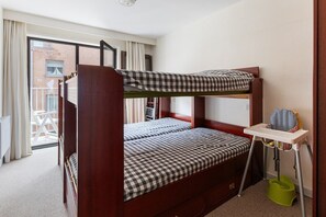 Een slaapkamer met een stapelbed, een geruit beddegoed, een klein tafeltje met een stoel en een groen po.