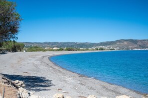 A coastal road leading to a beach with clear blue water, a rocky shoreline, and distant hills. - Natalia s Apartment in Tavronitis (Platanias)