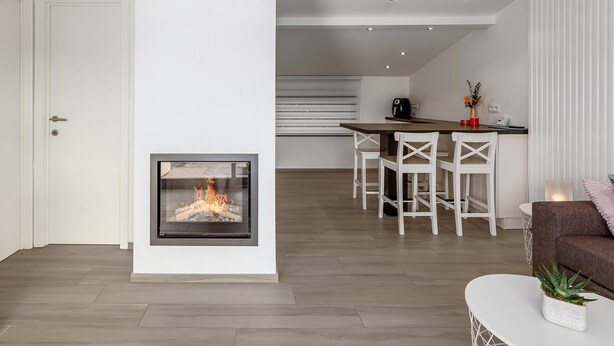 Una sala de estar moderna con chimenea, un comedor con sillas blancas y una cocina al fondo.