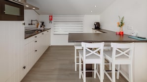 Una cocina moderna con armarios blancos, una encimera oscura y un horno empotrado. Hay dos sillas blancas en la isla, y una planta pequeña sobre la encimera.