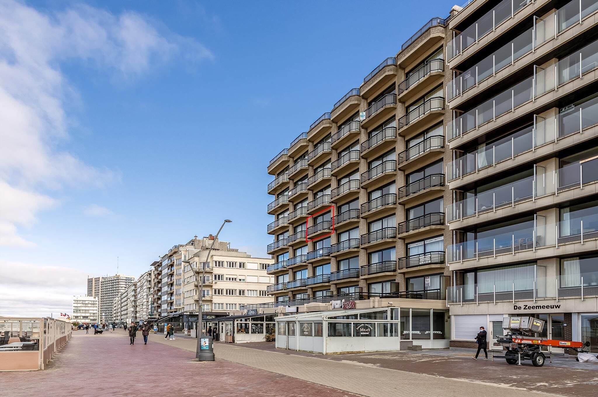 Un edificio de varios pisos con balcones, una cafetería y una tienda llamada 'De Zeemeeuw'.