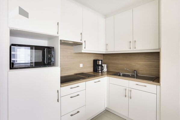 A modern kitchen with white cabinets, a built-in microwave, a coffee maker, and a sink.