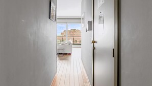 A narrow hallway with wooden flooring leading to a room with a desk and a window. - LONG ISLAND 19, B52 + G (Oostduinkerke)