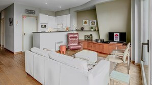 A modern living room with a white sofa, a red leather chair, a small table, and a TV. - LONG ISLAND 19, B52 + G (Oostduinkerke)