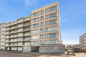 Un edificio de varios pisos con balcones, una tienda en la planta baja y un estacionamiento.