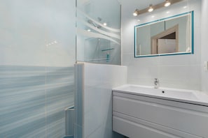 Un baño moderno con cabina de ducha de vidrio, un lavabo blanco y un espejo con marco azul.