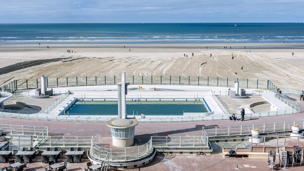 Uma praia com piscina, uma torre de salva-vidas e uma área de areia.