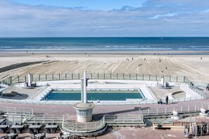 A beach with a swimming pool, a lifeguard tower, and a sandy area.