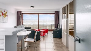 Quarto moderno com área de refeições, dois sofás, uma mesa pequena e vista para o mar através de grandes janelas.