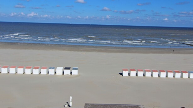 A beach with white and red barriers, a clear sky, and the ocean in the background.