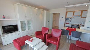 A modern living room with red leather sofas, a white TV stand, and a kitchen area with a microwave and stove.