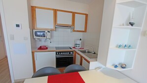 A compact kitchen with a microwave, oven, and coffee maker. There is a small sink and a shelf with decorative items.
