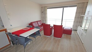 A modern hotel room with a dining area, red furniture, and large windows.